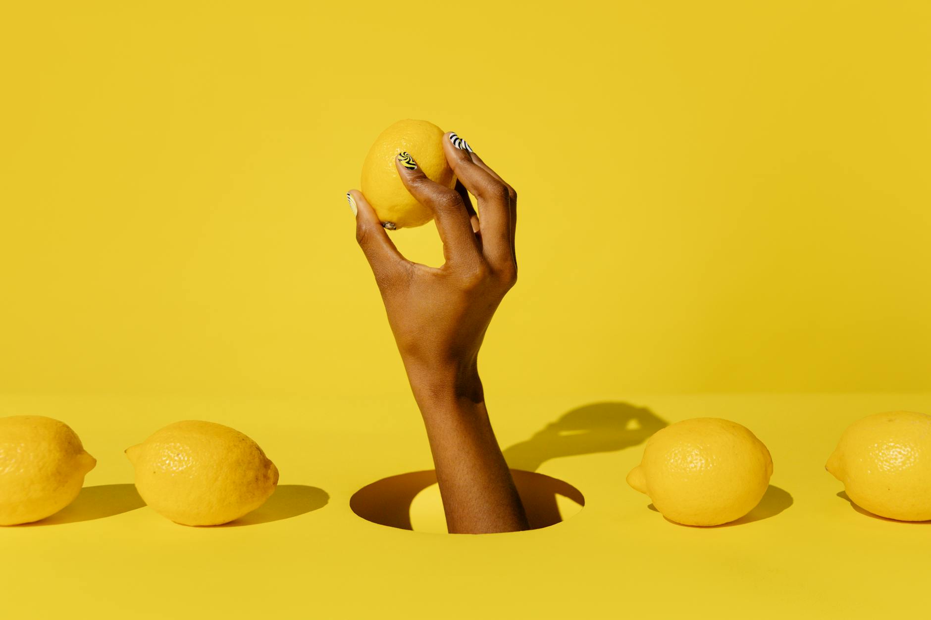 Hand holding a fresh lemon against a bright yellow background symbolizing the delicate nature of sensitive clitoral tissue