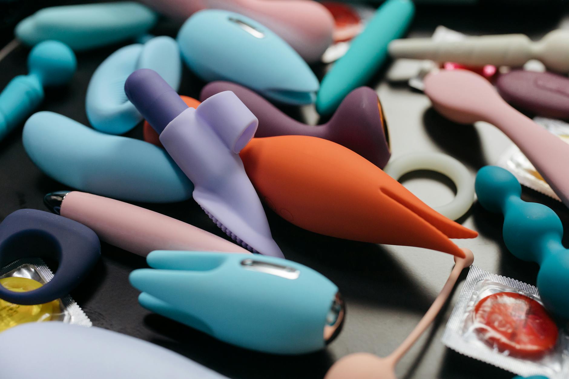 Two hands holding pink and blue silicone vibrators against a soft pastel background.