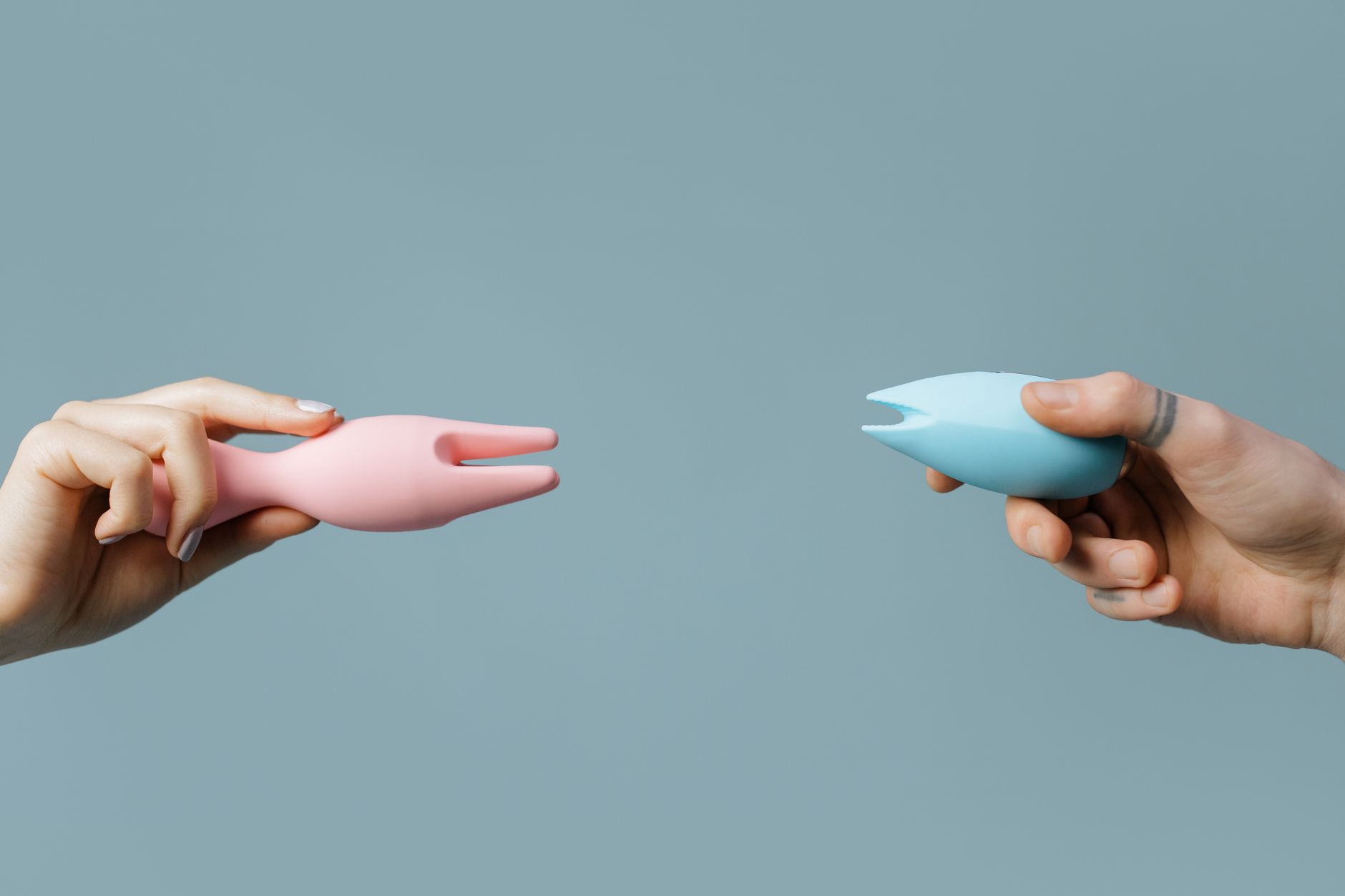 Two hands holding vibrators against a pastel background, representing intimate connection