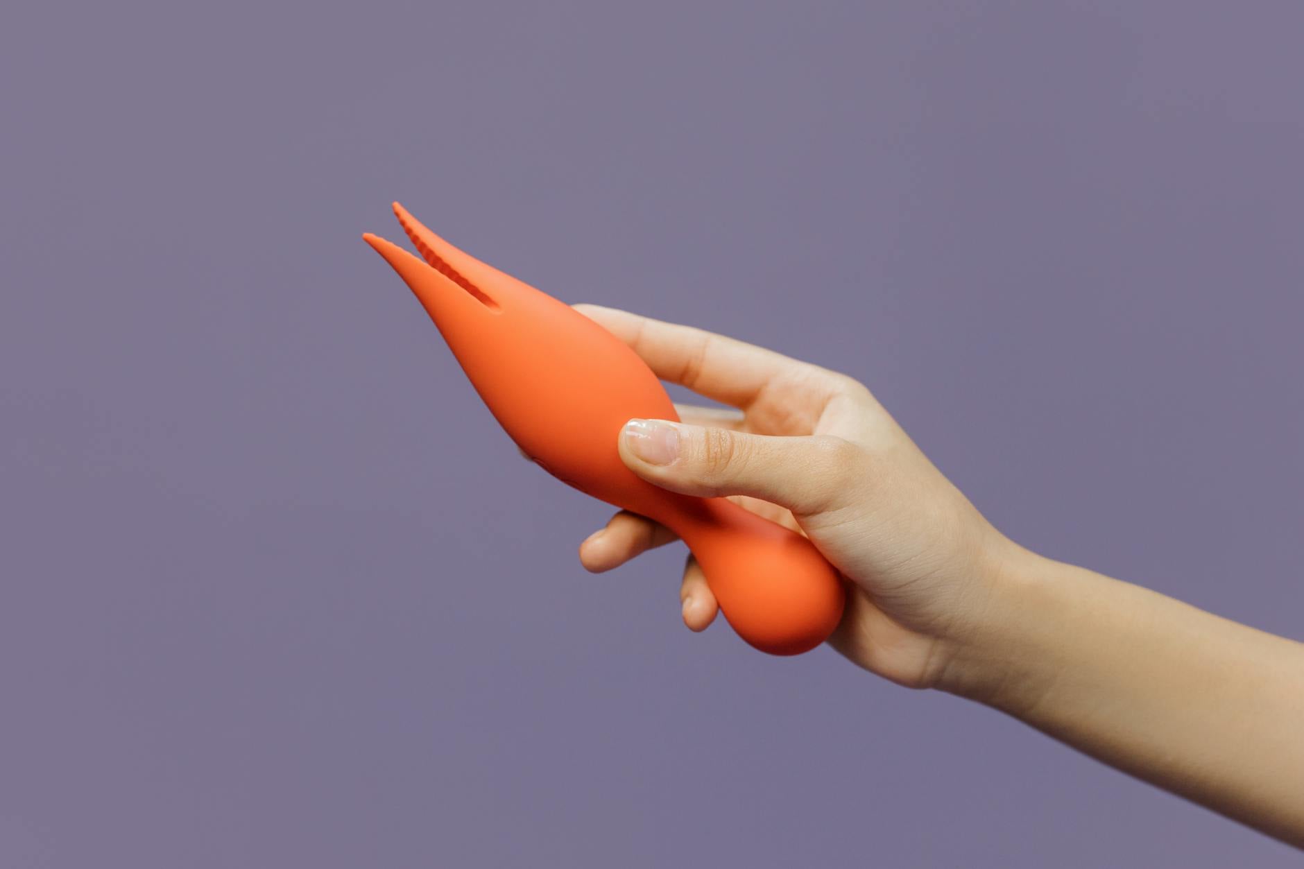 A hand holding The Lem clitoral vibrator against a minimalistic purple backdrop, showcasing modern sensuality.