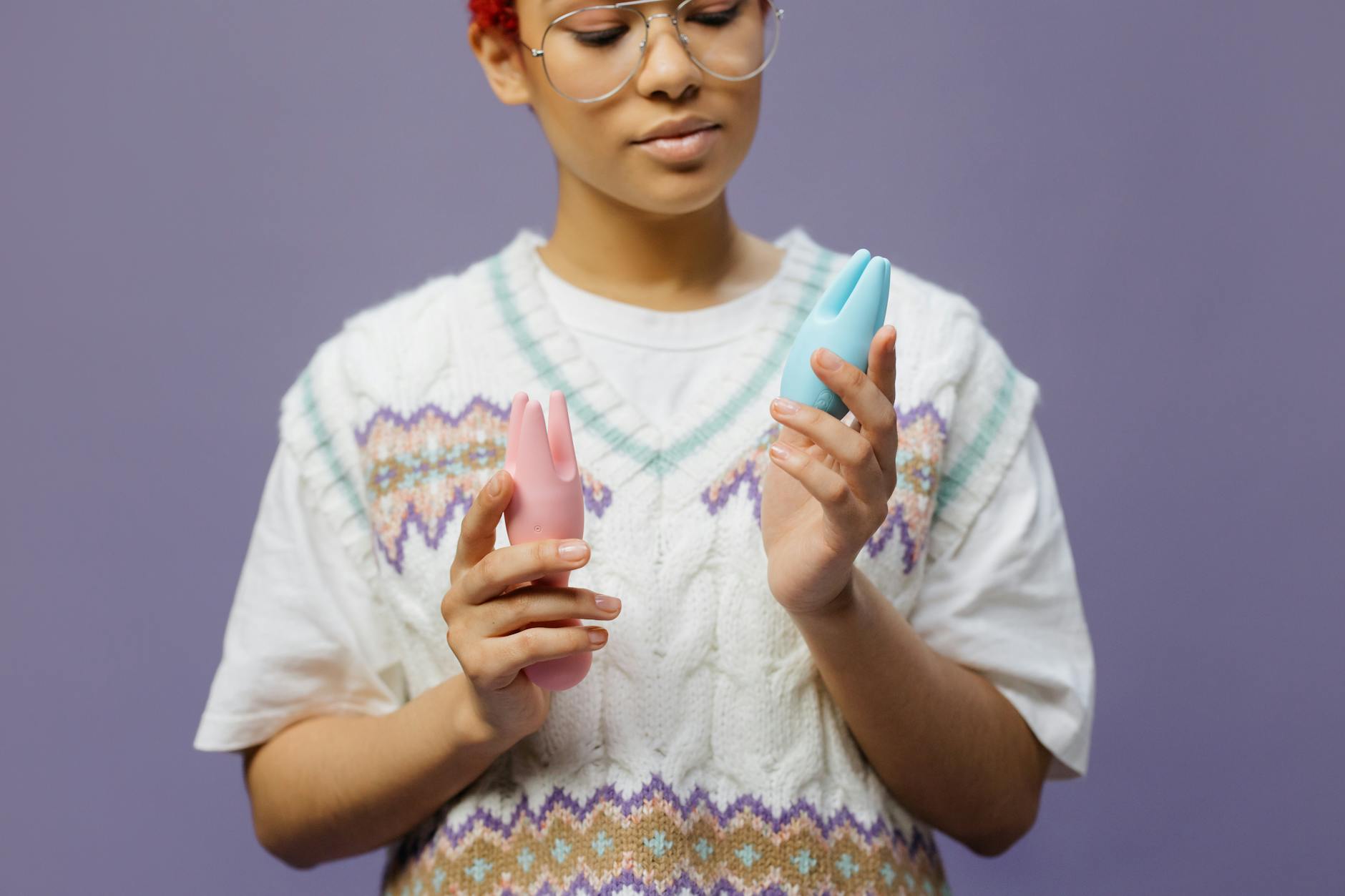 Woman holding blue and pink clitoral vibrators in contemplative pose